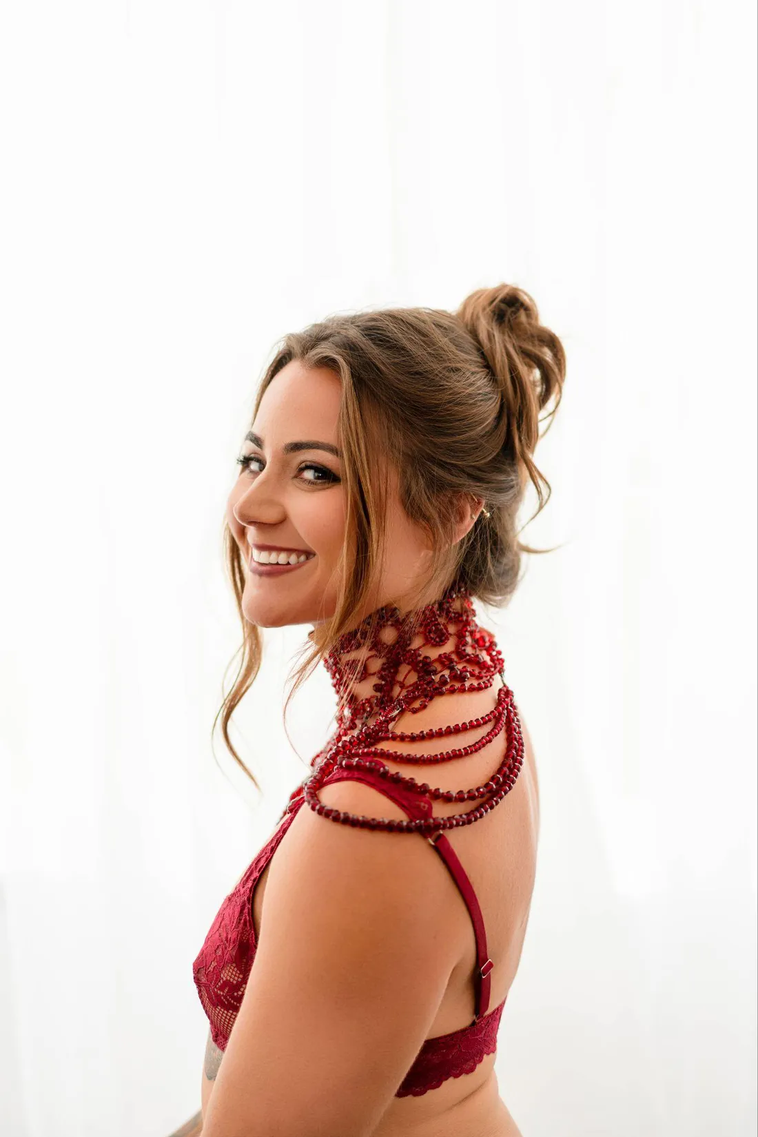 Helena Herndon in red lace lingerie and a beaded red collar, smiling over her shoulder