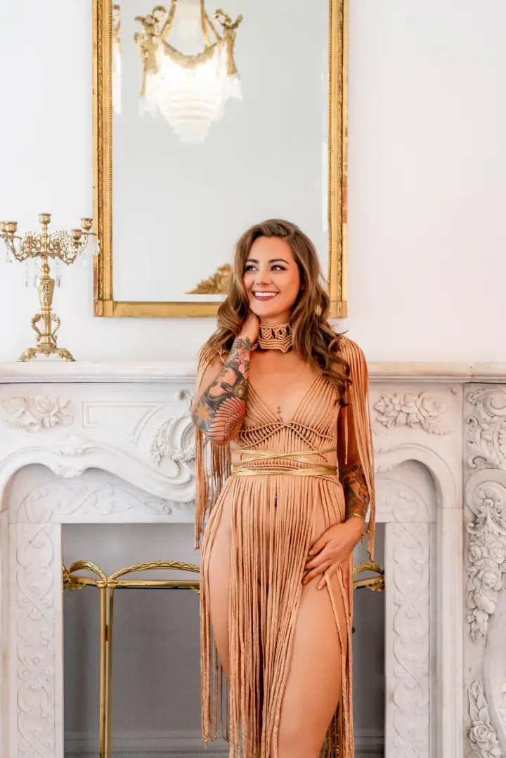 Helena Herndon in a gold fringed gown, smiling in front of a marble fireplace and gilded mirror