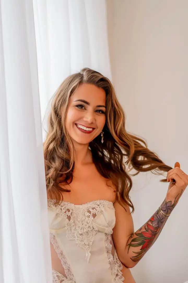 Helena Herndon smiling in a cream lace bodysuit beside white curtains